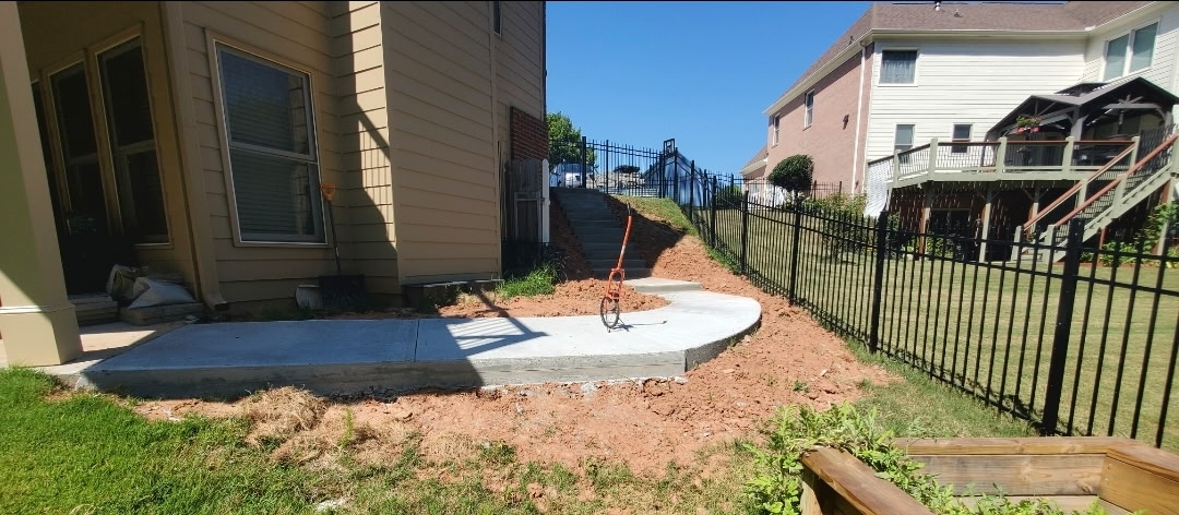 Concrete patio pad bordered by a black iron fence