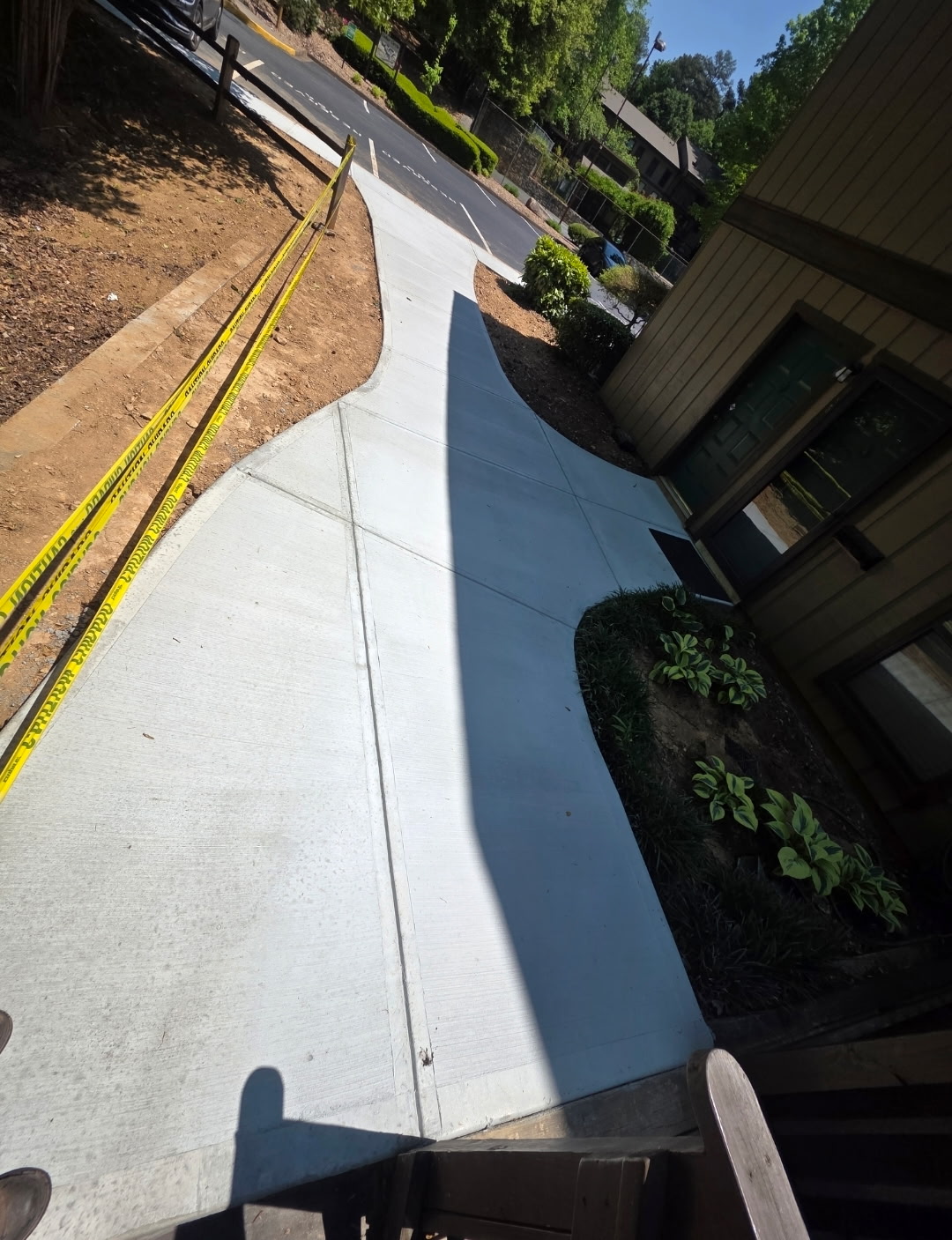 Freshly poured concrete walkway winding between building and fence