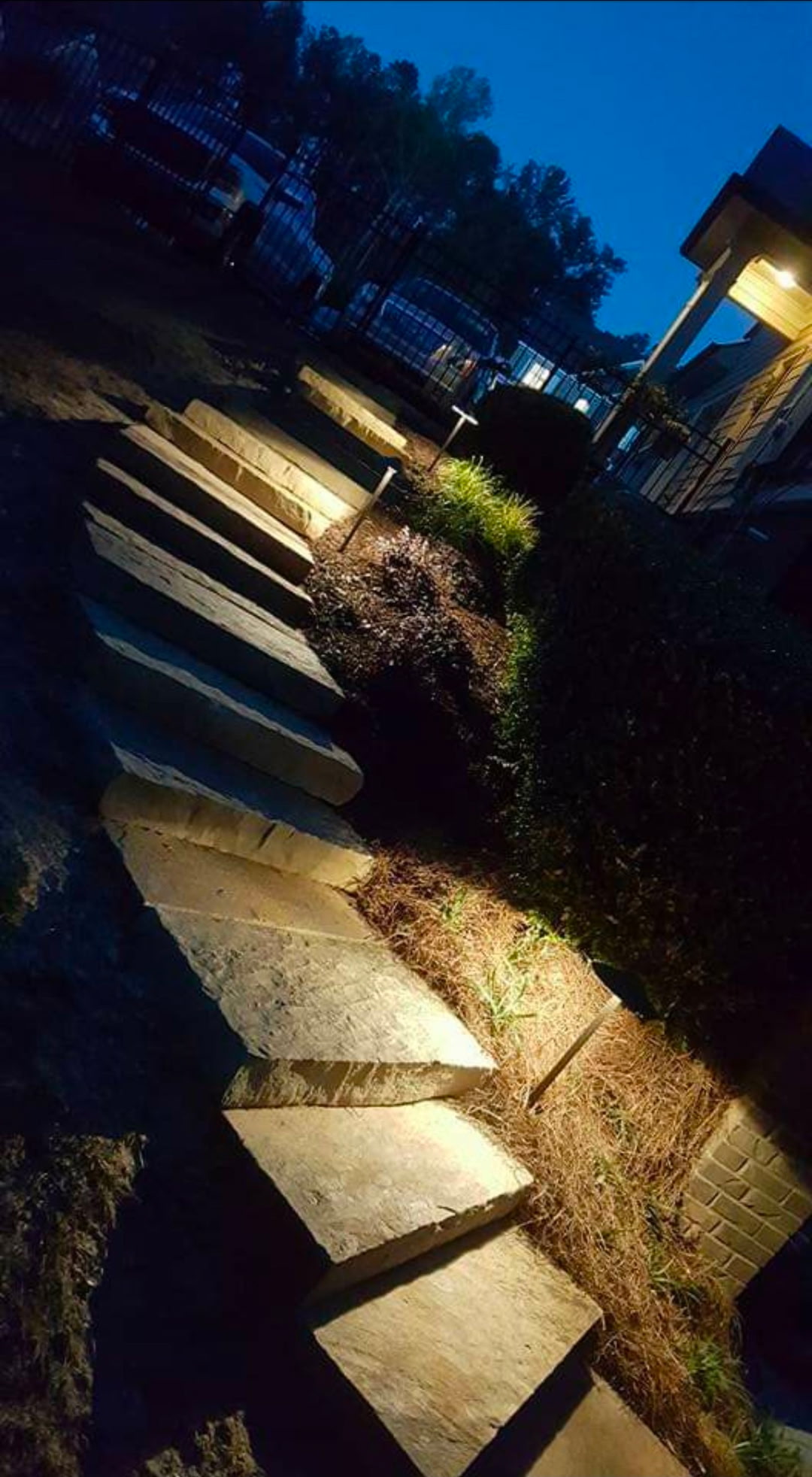 Natural stone-slab staircase lit by warm low-voltage path lighting at dusk
