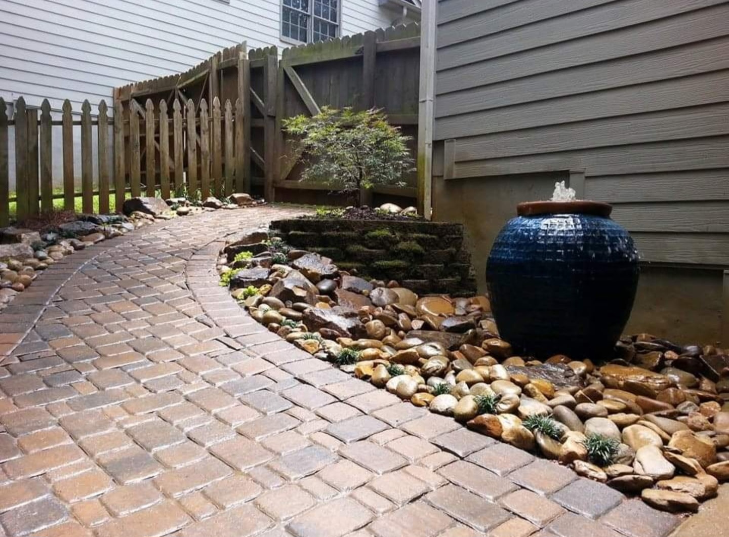 Dark blue glazed jar fountain along a curved paver path