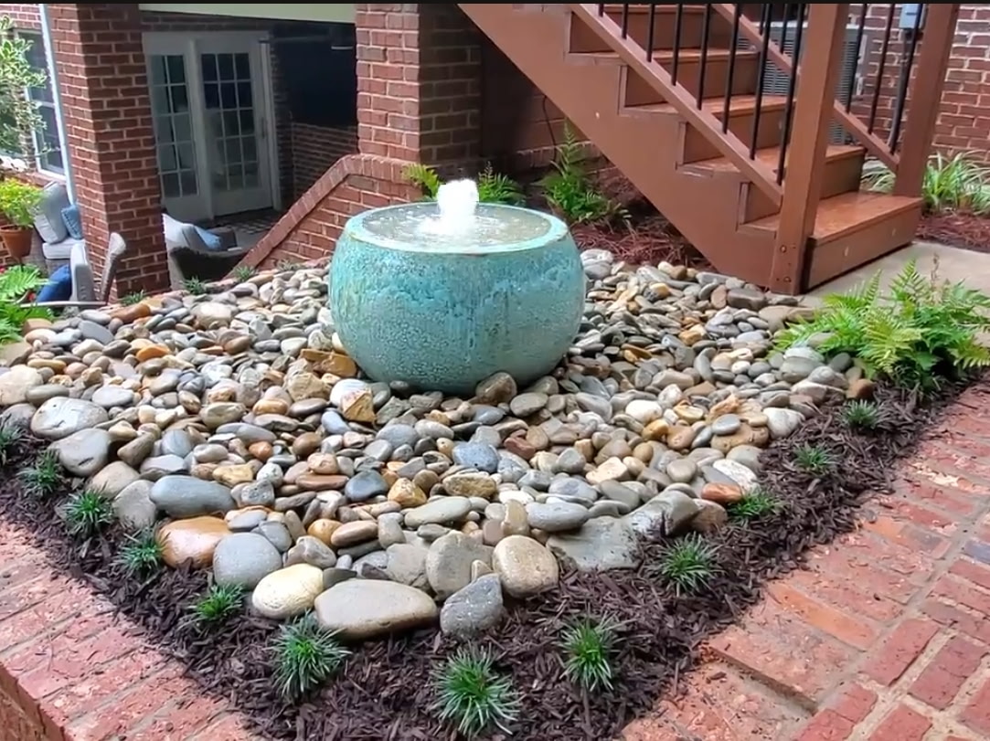 Teal spherical fountain bubbling in a river-rock bed